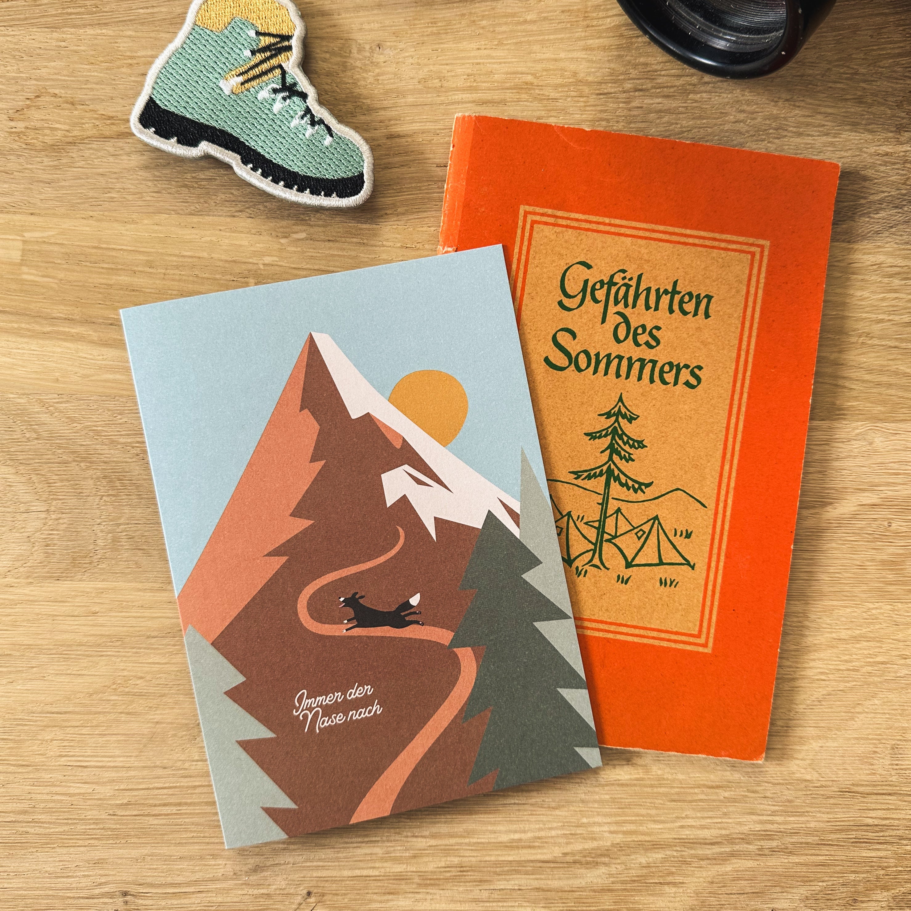 Grußkarte von Roadtyping mit der Illustration eines kleinen Hundes, der auf einem Weg vor einem großen Berg steht. Darüber steht der Schriftzug "Immer der Nase nach".