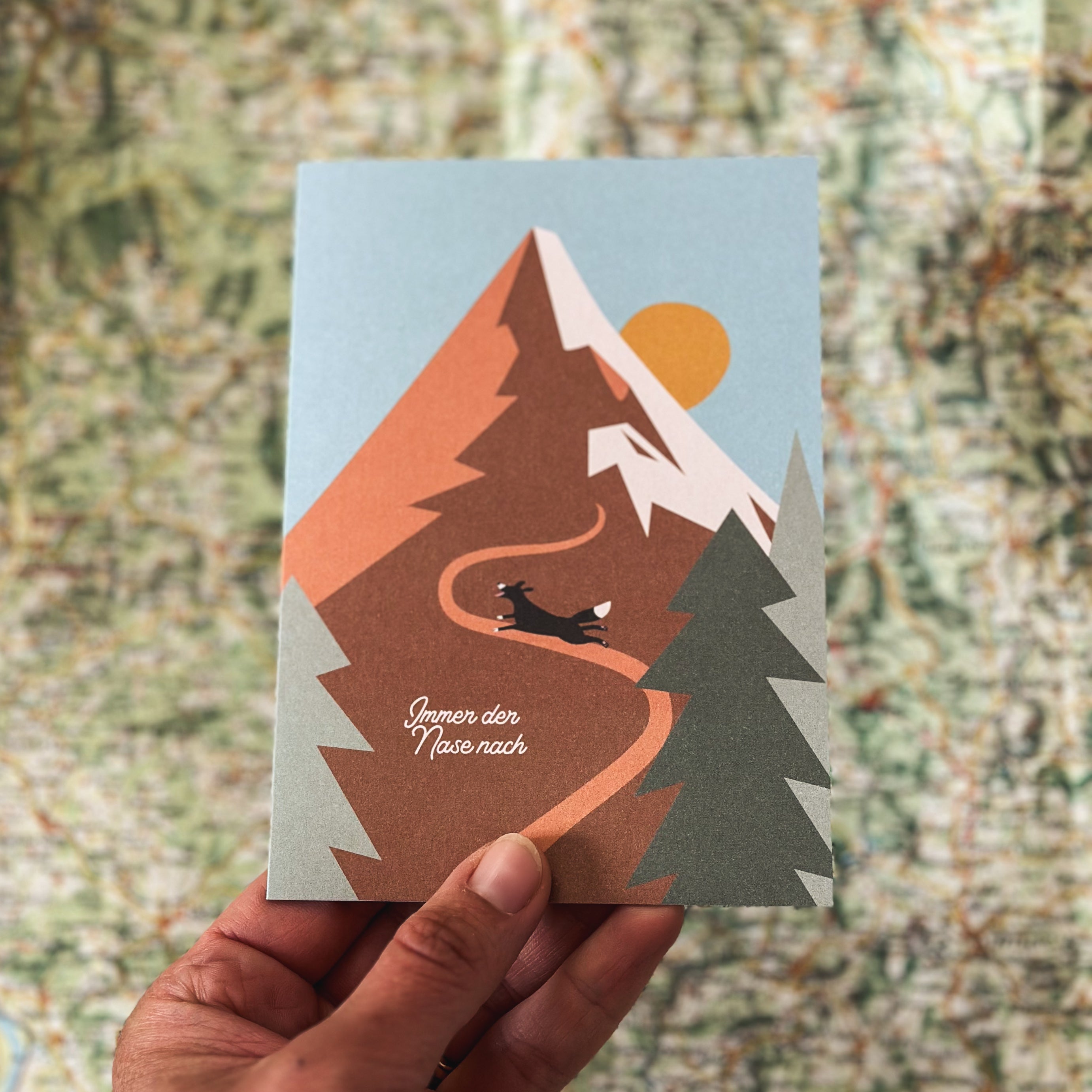 Grußkarte von Roadtyping mit der Illustration eines kleinen Hundes, der auf einem Weg vor einem großen Berg steht. Darüber steht der Schriftzug "Immer der Nase nach".