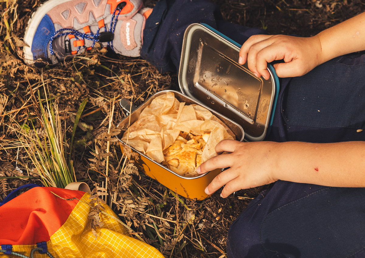 Kind öffnet den Deckel einer Lunchbox mit Apfelkuchen drin