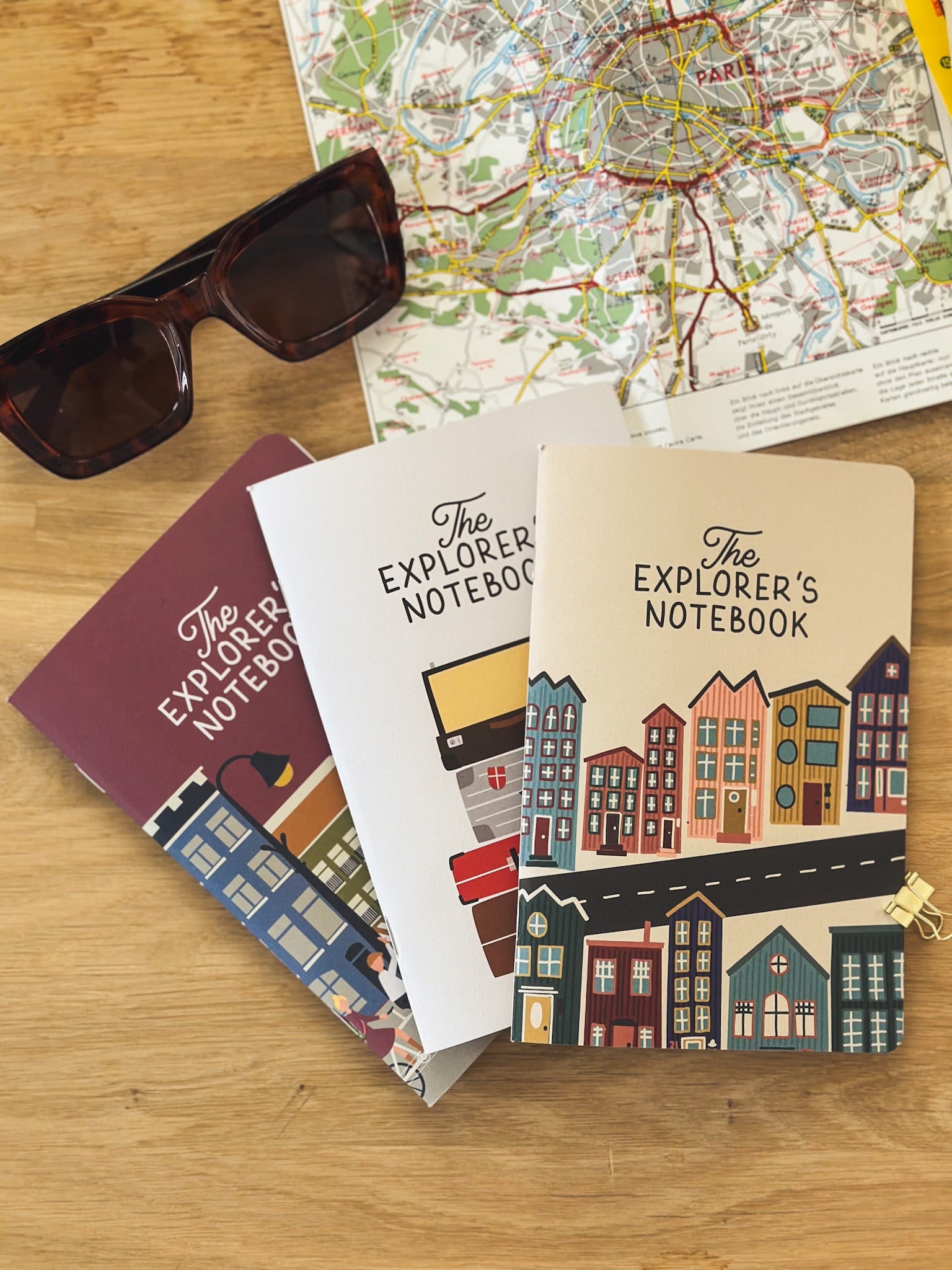 Drei Reisetageücher The Explorers Notebook Band 5 liegt offen auf einem Tisch neben Brille und Stadtplan